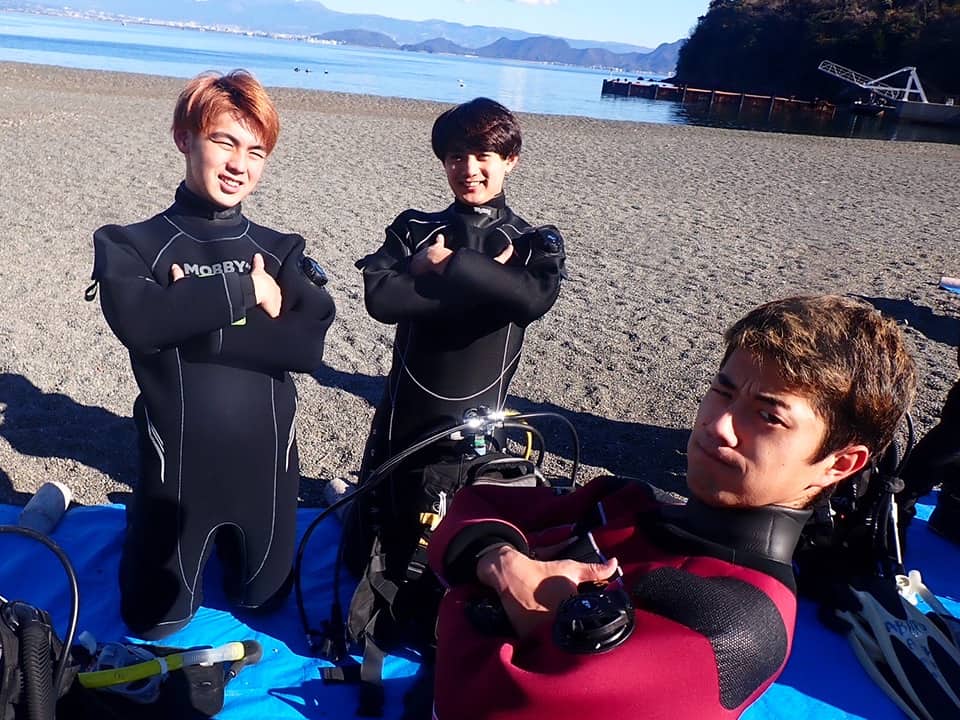 砂浜でポーズを取る三人の学生ダイバー